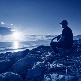 Firdaus R seated on a rocky shoreline overlooking the ocean